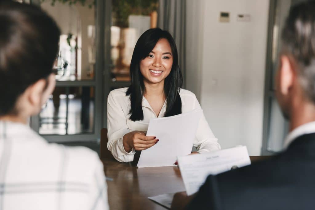 Business, career and recruitment concept - young asian woman smiling and holding resume while interviewing as candidate for job in big company